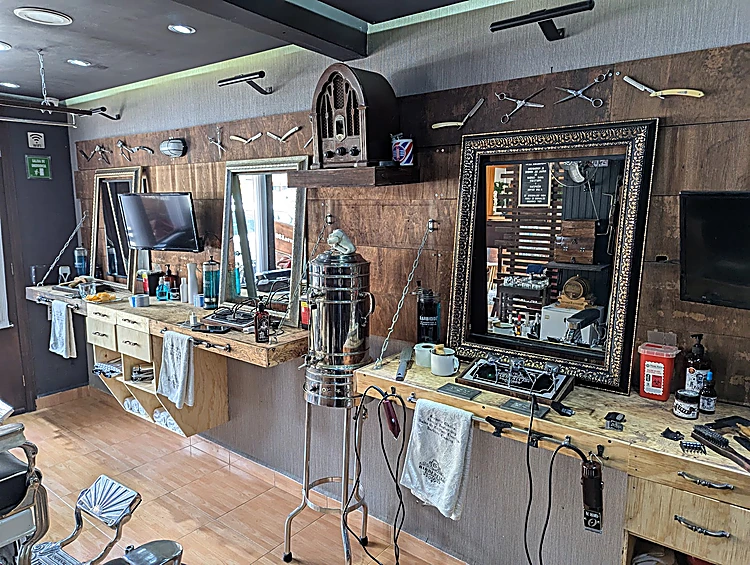 Rincón de barbería con estaciones de madera, espejo grande de marco tallado, radio antigua en la pared y toallas colgadas