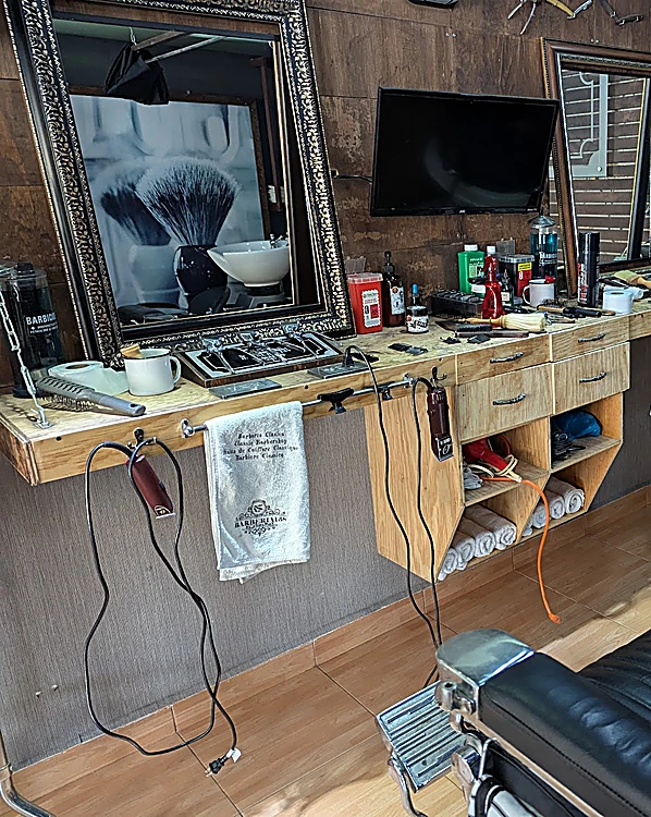 Estación de barbería con espejo de marco oscuro, herramientas, toalla colgada y sillón negro
