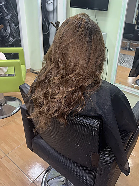 Cabello largo castaño con ondas y reflejos claros, de espaldas en el sillón, con un sillón verde lima al fondo