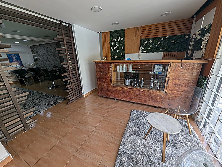 Recepción con mostrador de madera, muro de plantas verdes, tapete gris y una mesita blanca