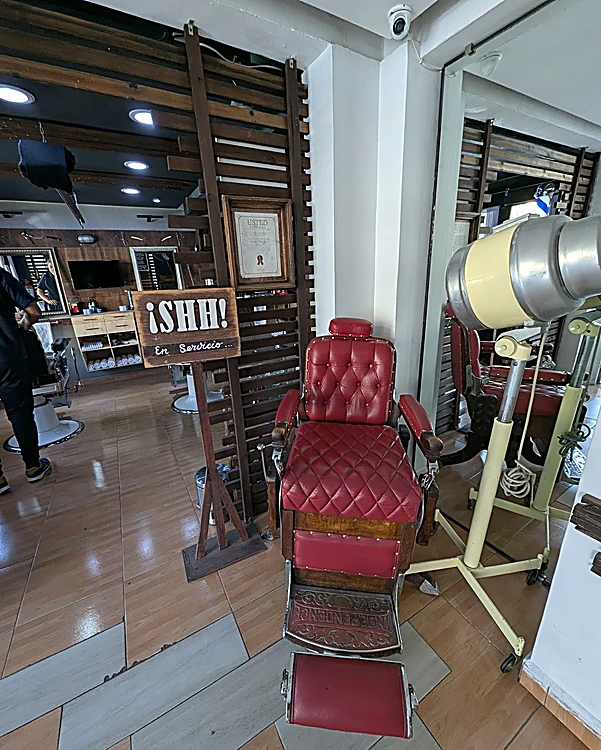 Sillón rojo capitoné junto a un letrero de madera que dice ¡SHH!, con persianas de madera detrás